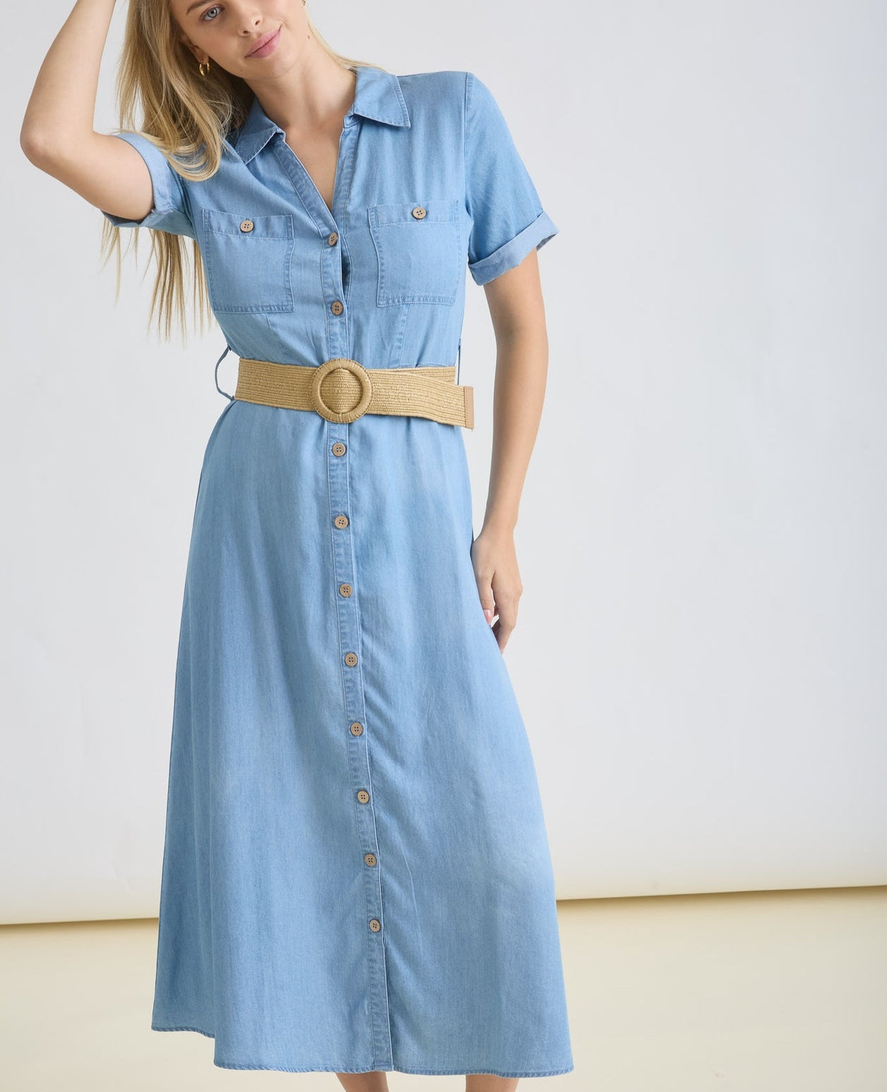 Woman wearing a light blue dress with a beige belt against a white background