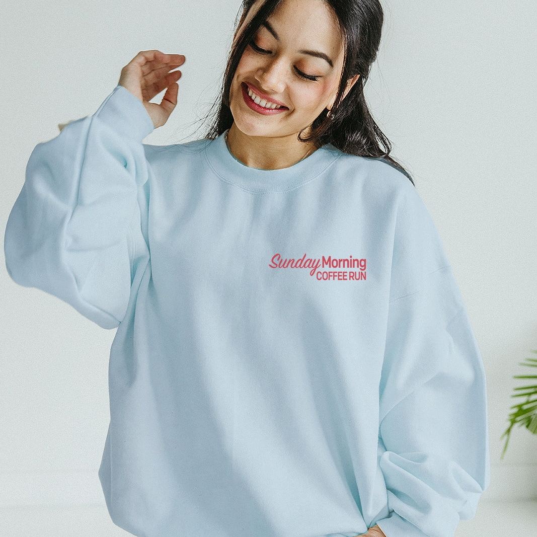 Woman wearing a light blue sweatshirt with 'Sunday Morning Coffee' text, standing against a white background.