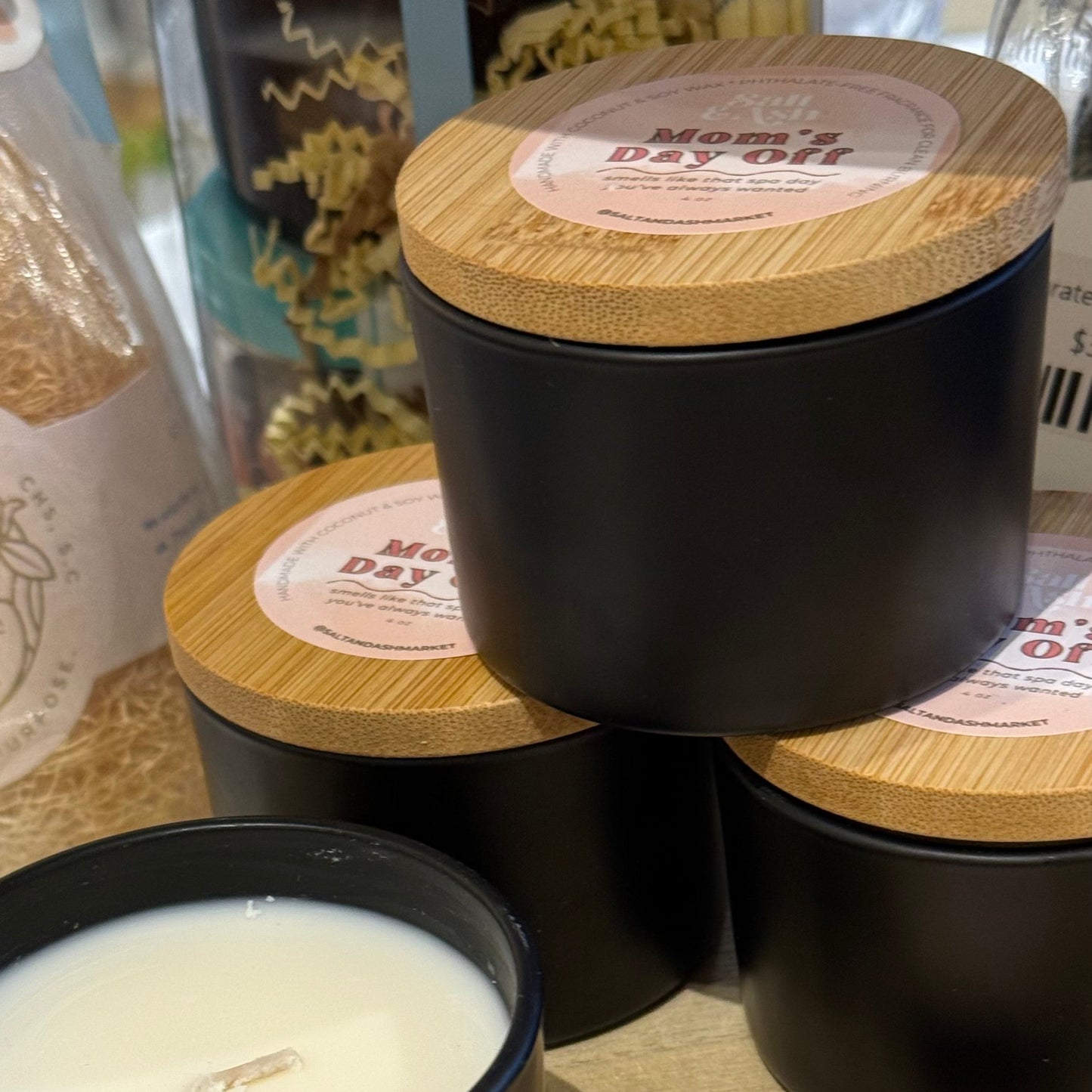 Candles with 'Mom's Day Off' labels on a wooden surface