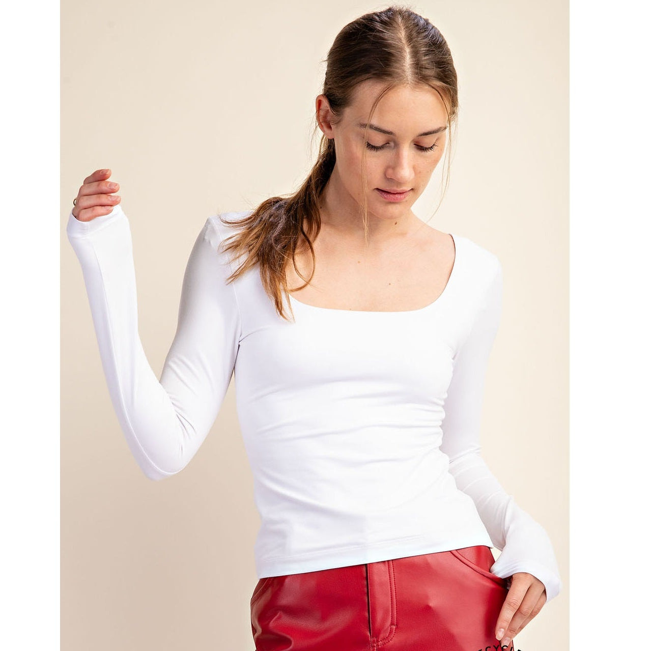 Woman wearing a white long-sleeve top and red pants on a beige background